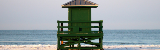 Green lifeguard tower on a sandy beach with calm ocean waves in the background.